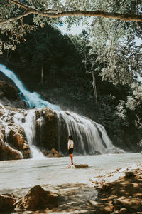 Man standing on rock against waterfall