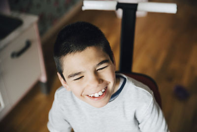 High angle view of happy disabled boy looking away while sitting on wheelchair at home