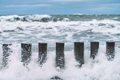 High wooden breakwaters in splashing sea waves, beautiful cloudy sky, close up 