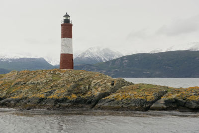 Lighthouse amidst buildings and mountains against sky