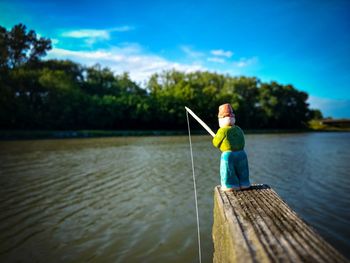 Man fishing on lake against blue sky