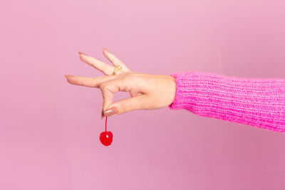 Female hand wearing pink sweater and holding a cherry. light pink background.