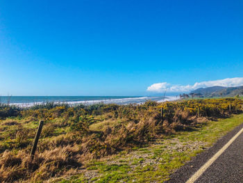Scenic view of road by sea against blue sky