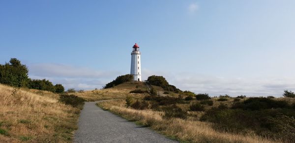 Lighthouse on field by building against sky