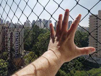 Cropped image of hand against chainlink fence