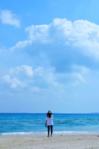 Rear view of woman standing on beach against sky