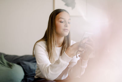 Teenage girl using social media on smart phone while sitting at home