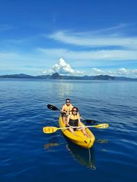 Couple kayaking on lake against blue sky