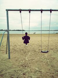 Rear view of woman playing on swing at beach