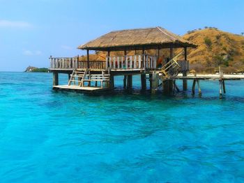 Stilt house by sea against blue sky