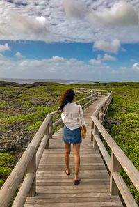 Rear view of woman standing on railing against sky