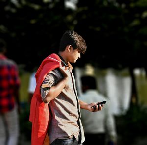 Side view of young man using phone on footpath