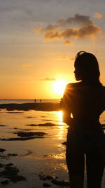 Silhouette woman on beach against sky during sunset