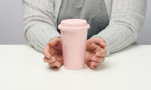 Woman in gray clothes holds a pink ceramic cup, woman sits at a white table, start of the day, morn