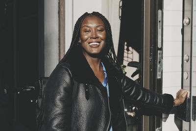 Portrait of smiling businesswoman wearing leather jacket while entering at office