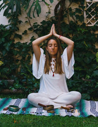 Full length of young woman meditating while sitting outdoors