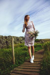 Side view of young woman standing on boardwalk against sky