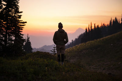 Rear view of man standing on field against sky during sunset