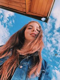 Low angle portrait of smiling young woman standing against sky