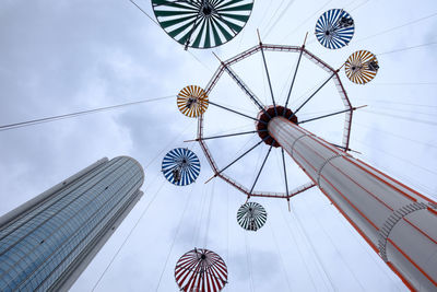 Low angle view of chain swing ride by building against cloudy sky