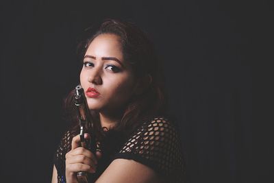 Portrait of beautiful woman holding handgun in darkroom