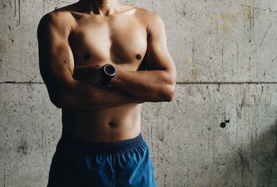 Close-up of shirtless man holding camera while standing against wall