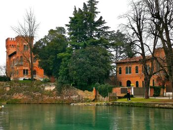 Trees and buildings by lake against sky