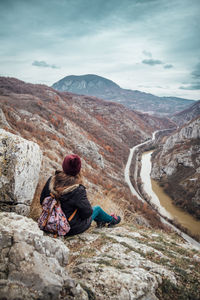 Rear view of man sitting on rock against sky