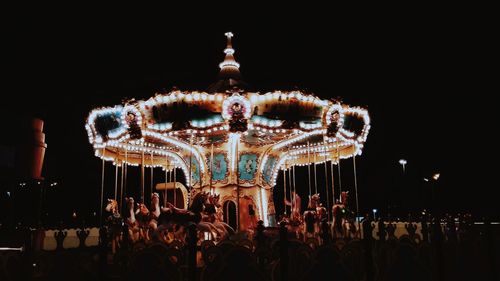 Illuminated carousel at amusement park against sky at night