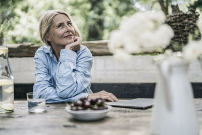 Mature woman sitting on terrace, with cherries on table