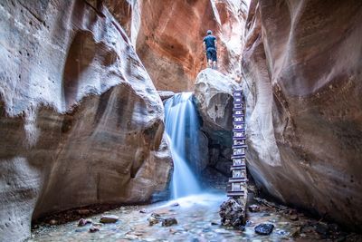 Low angle view of man standing on rock by waterfall