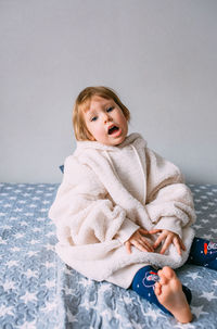 Cute child y on the bed in cozy adult clothes and a hat with earflaps.