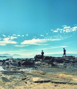 Men standing on rocks by sea against sky