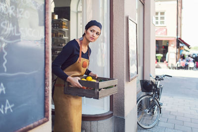 Owner looking away while carrying vegetable crate at entrance of grocery store