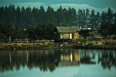 House by lake and trees against sky