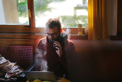 Man smoking electronic cigarette while using laptop at home