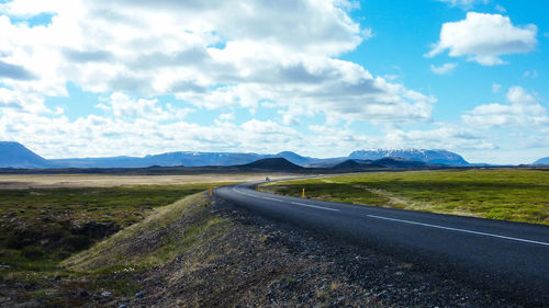 Country road along landscape and mountains against sky