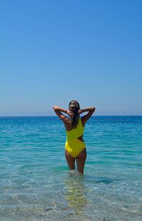 Rear view of woman standing in sea against clear blue sky
