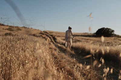 Rear view of man walking on field against sky