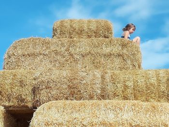 Young woman with hay bales on field against sky