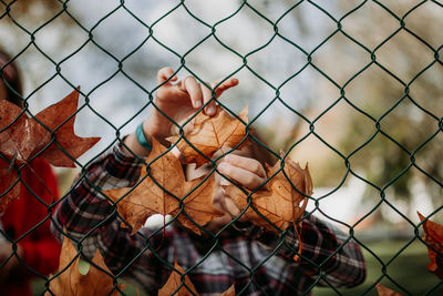 Baby girl holding leaves behind chainlink fence during autumn