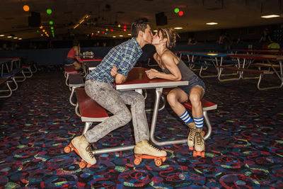 Couple wearing roller skates kissing while sitting at table in club