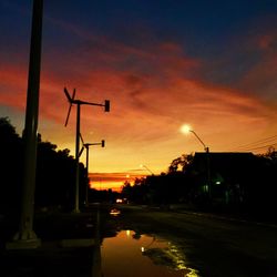 Road by silhouette trees against sky at sunset