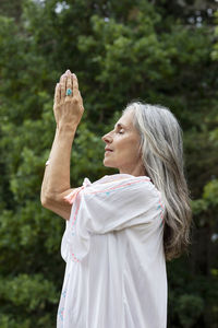 Mature woman meditating with hands clasped in forest