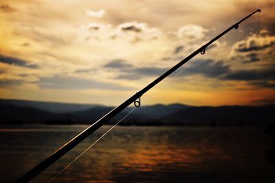 Silhouette fishing rod on sea against sky during sunset