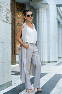 Successful woman posing in a pantsuit and sunglasses near a building
