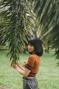 Side view of thoughtful young woman standing against trees in park
