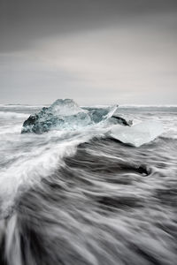 Striking block of ice on a black beach with surf, with returning water reflection on the wet sand