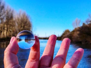 Cropped image of hand holding crystal ball against river