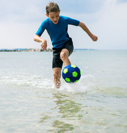 Full length of boy playing soccer ball in water at beach